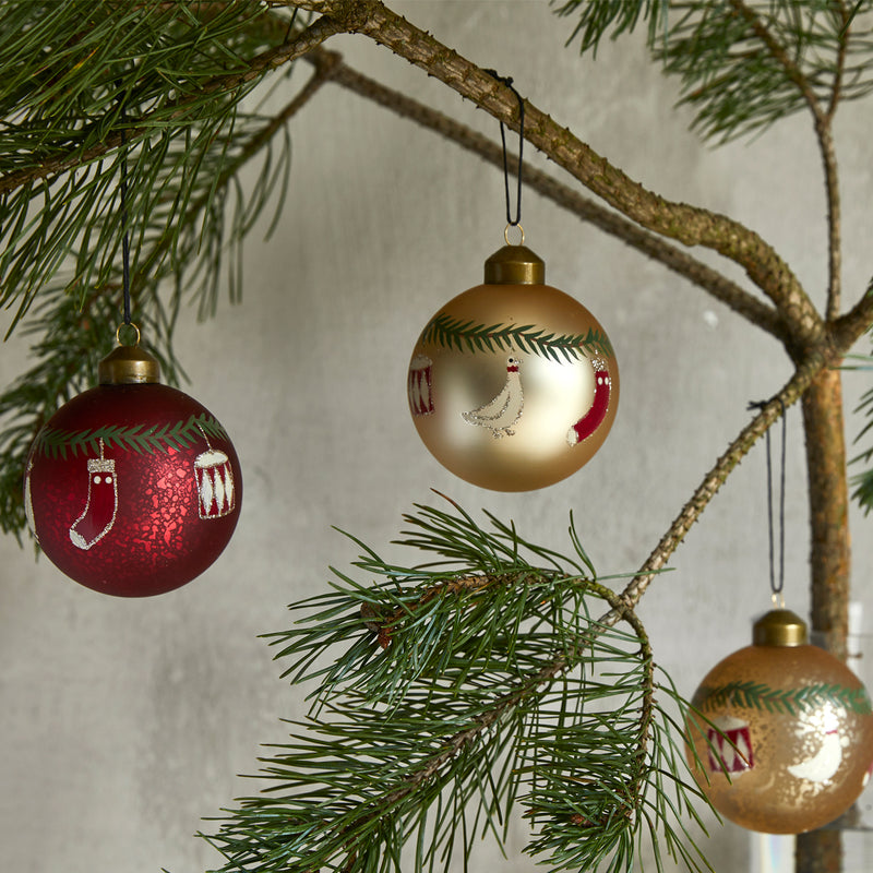 Røde julekugler med Dannebrog på et bord sammen med garderfigurer, grangrene, en kogle og en sølvfarvet julekugle.