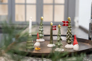 Grønne keramikjuletræer med gyldne stjerner og Dannebrog på et rundt fad sammen med en lysestage og små julefigurer med røde huer.