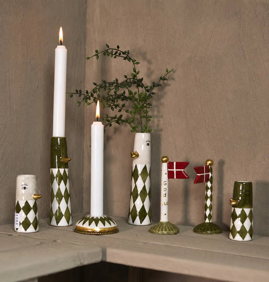 Juleflag med grøn fod og God jul-tekst på en hylde med grønne og hvide dekorationer og tændte lys.
